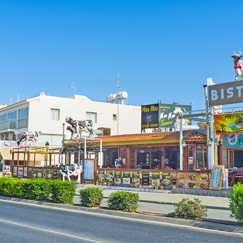 AYIA NAPA, CYPRUS - AUGUST 1, 2014: The scenic cafe decorated with the numerous sculptures of cows, located on the central tourist street, on August 1 in Ayia Napa.